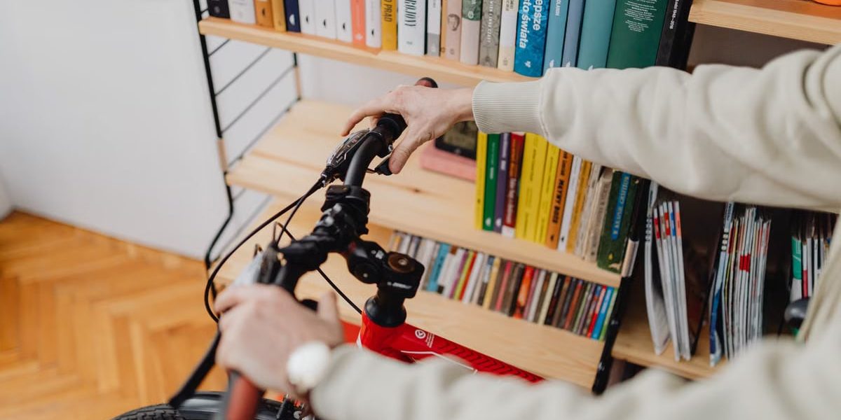 An indoor scene featuring hands holding a bicycle handlebar against a backdrop of a bookshelves.