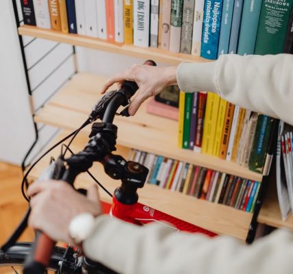 An indoor scene featuring hands holding a bicycle handlebar against a backdrop of a bookshelves.