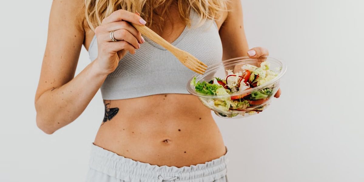 Young woman in sports attire holding a fresh salad bowl, promoting a healthy lifestyle.