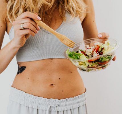 Young woman in sports attire holding a fresh salad bowl, promoting a healthy lifestyle.