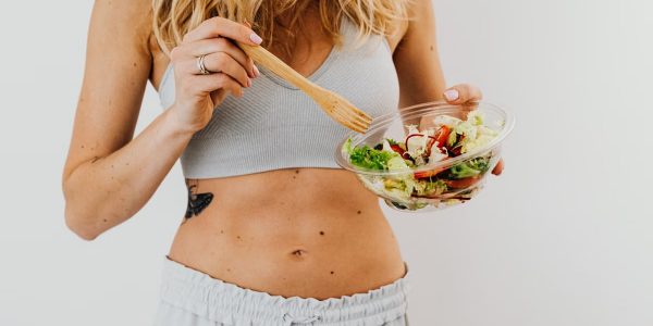 Young woman in sports attire holding a fresh salad bowl, promoting a healthy lifestyle.